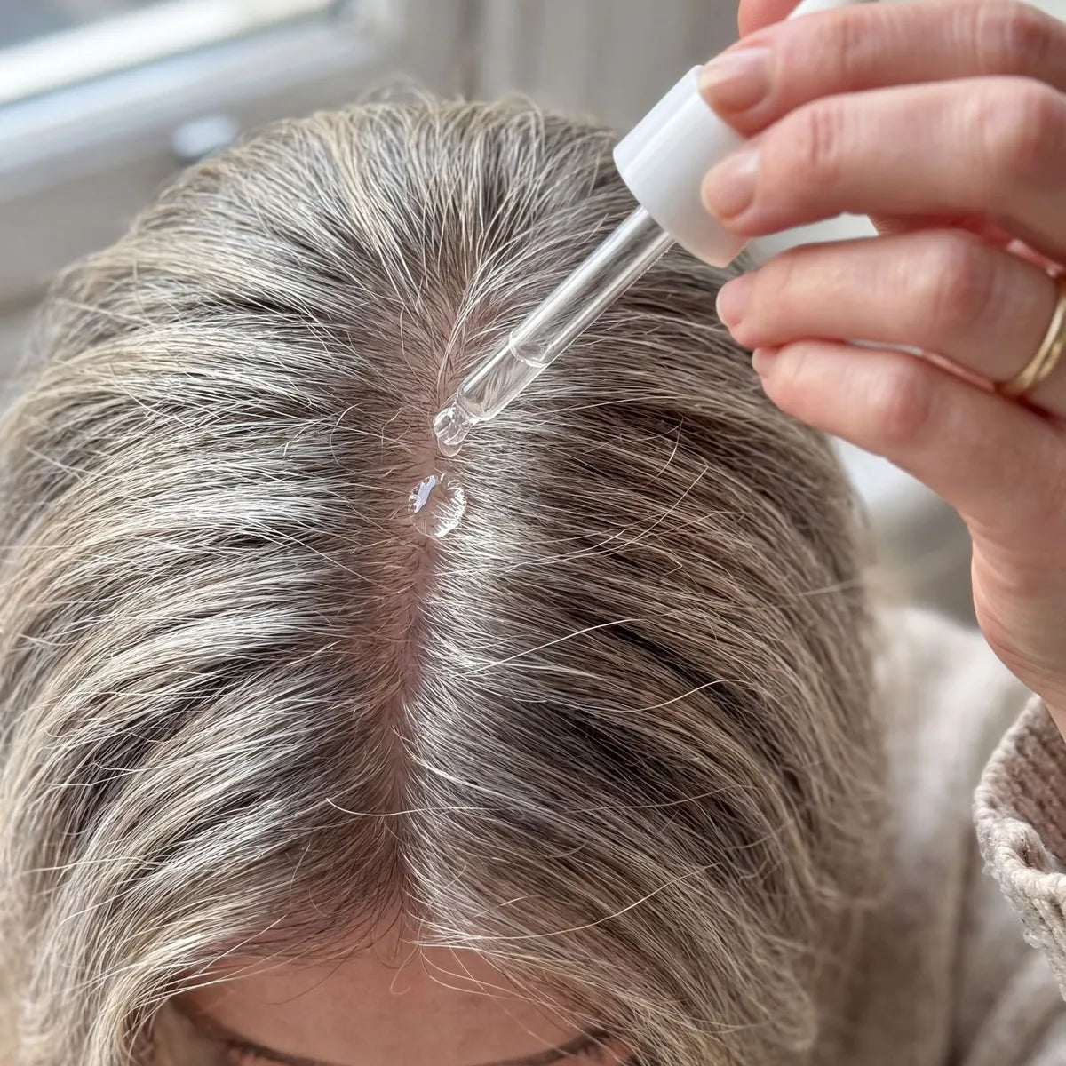 The dropper over a grey-blonde parting, the serum clear